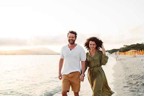 "coppia passeggia tenendosi per mano in spiaggia ad Alghero"