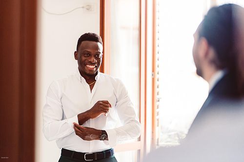 "invitato che si allaccia la camicia e guarda lo sposo"