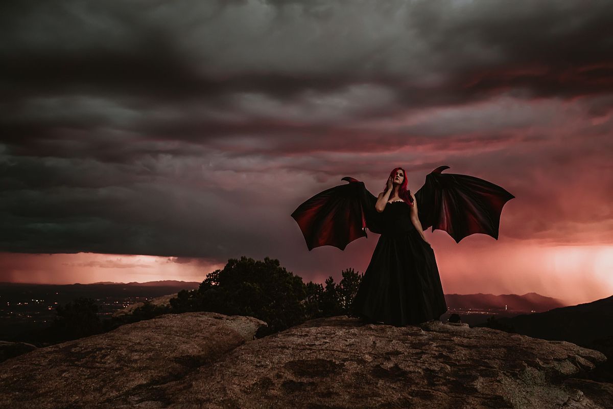 Empowering stormy-day portrait with woman wearing wings on a rugged mountain slope.
