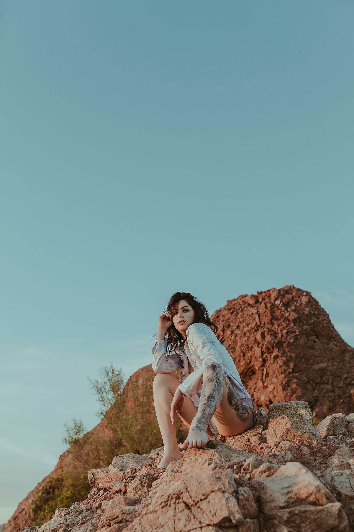 Casual and confident boudoir photo of a woman wearing an oversized white men’s shirt, posing at the top of a mountain surrounded by red rock formations in Arizona.