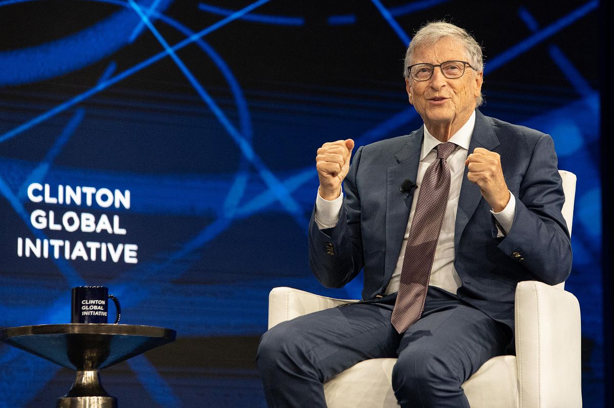 Keynote speaker gestures during a global conference session, with event branding on a blue stage backdrop—strong presence and authority.