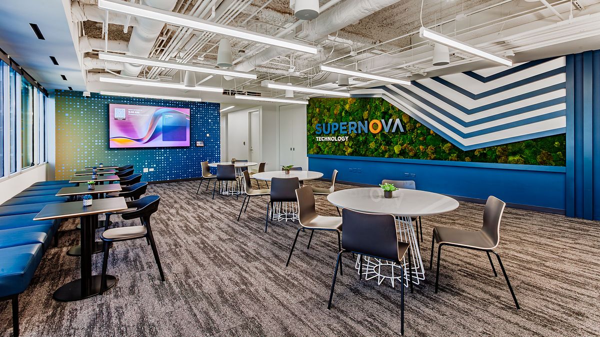 Modern Chicago office interior for Supernova Technology featuring a biophilic living wall, white collaboration tables, and industrial exposed ceilings.