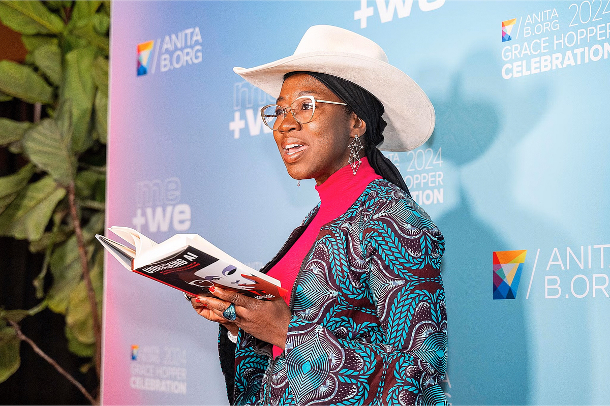 Corporate event photography capturing an AI ethics advocate reading from a book during a presentation at the Grace Hopper Celebration 2024 in Philadelphia, emphasizing leadership, diversity, and inclusion in the tech community.