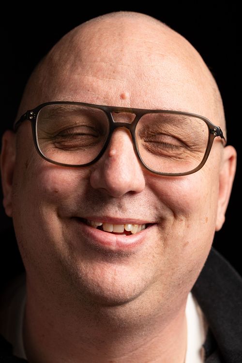 Leende man med glasögon i mjukt studioljus, autentiskt uttryck