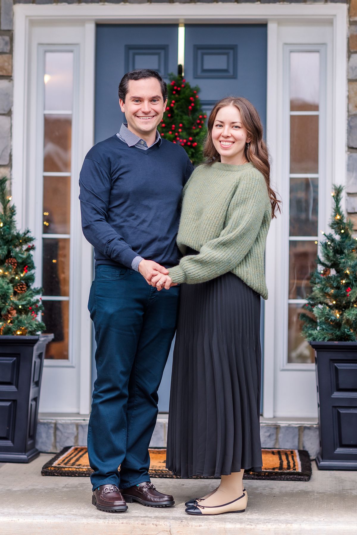Husband and wife on Christmas-decorated porch, smiling and holding hands with Cranberry Township, PA newborn photographer