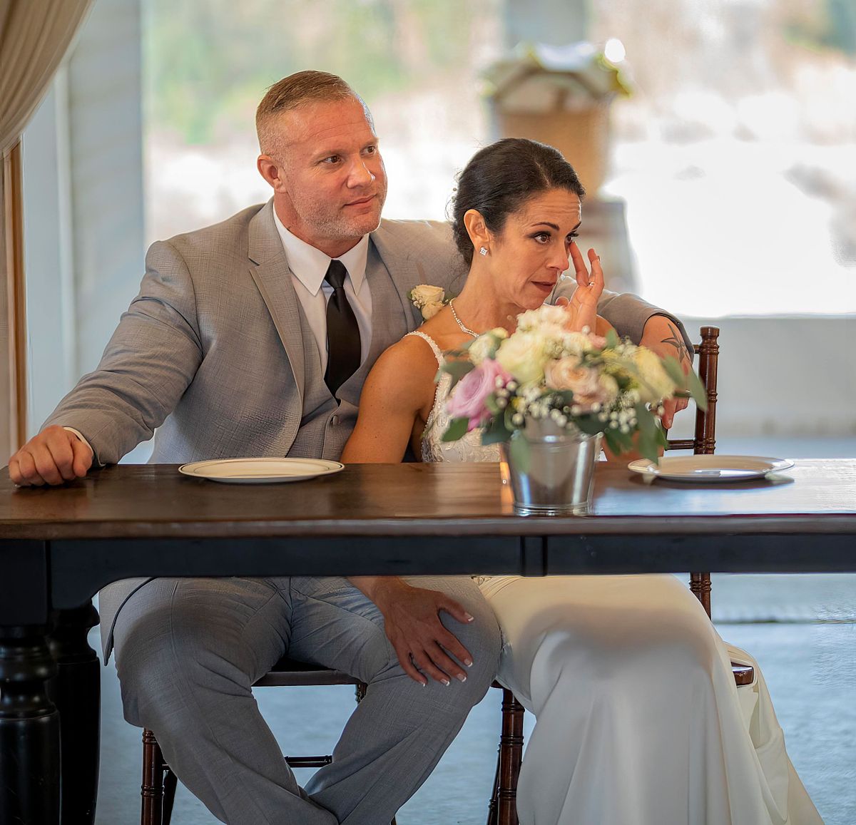 bride and groom sitting at the sweetheart's table listening to speeches, the bride is very emotional