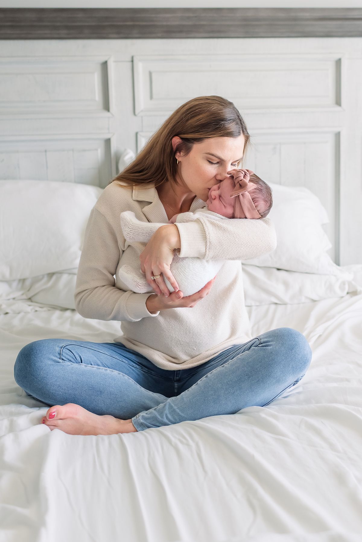 mother sitting criss cross on bed and kissing newborn baby girl on the cheek with cranberry township, pa newborn photographer