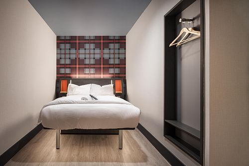 Interior view of a single room at the Easy Hotel Dublin, facing the bed. A feature wall with a red and grey geometric pattern is behind the bed. Built-in storage with coat hangers is visible on the right.