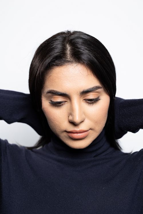 Studioporträtt av skådespelare med händerna bakom huvudet och mjuk blick, fotograferat mot ljus bakgrund.