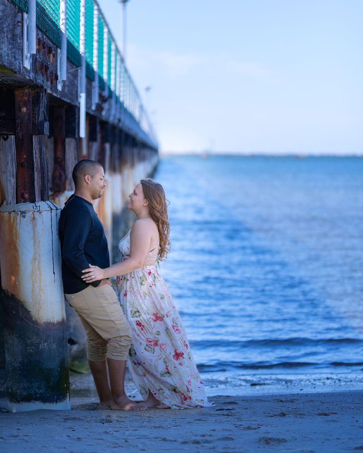 couple underneath the pier at cape henlopen embracing each other.