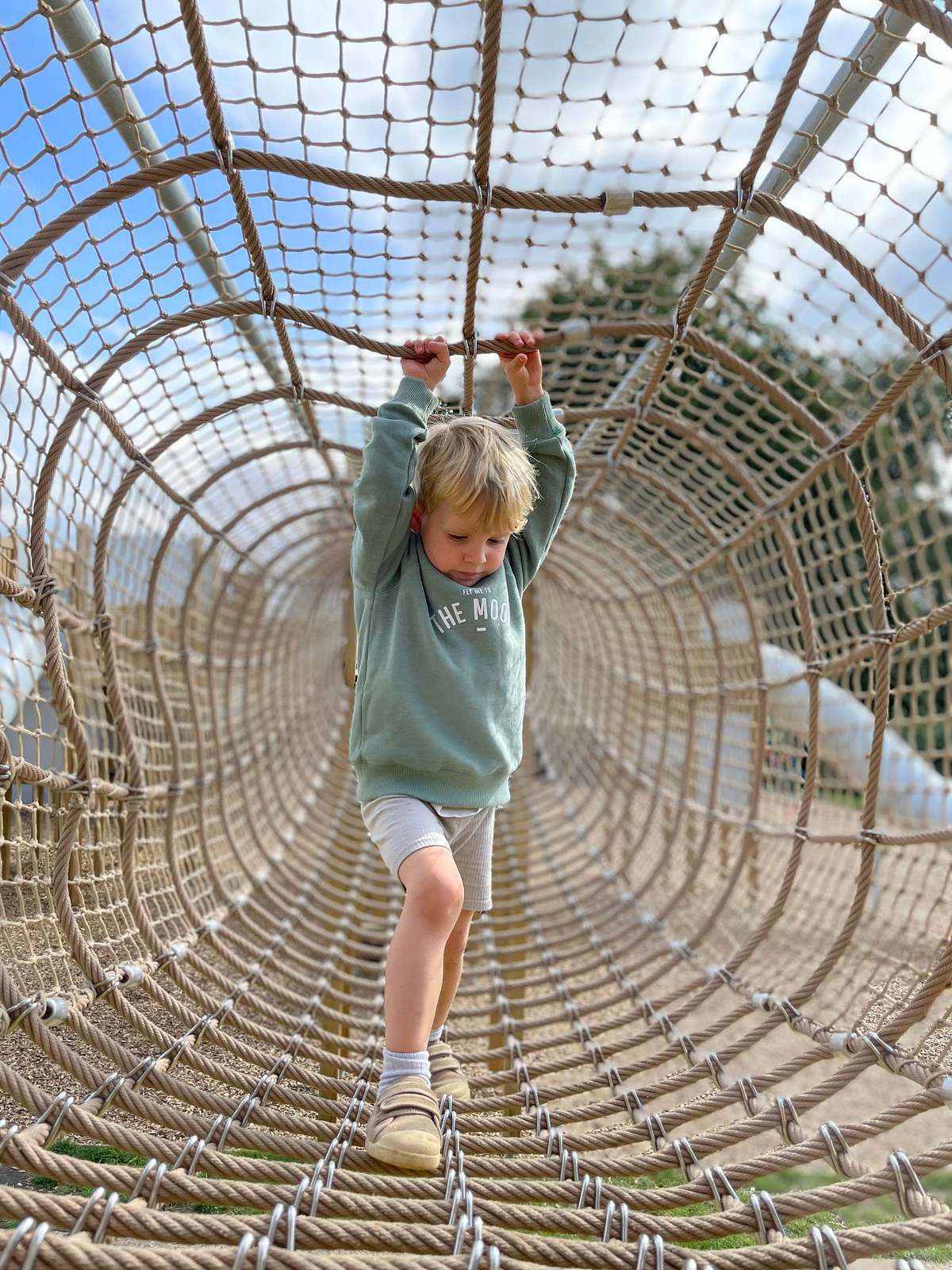 Child balancing on rope tunnel outdoor structure, lifestyle children's photography Northamptonshire