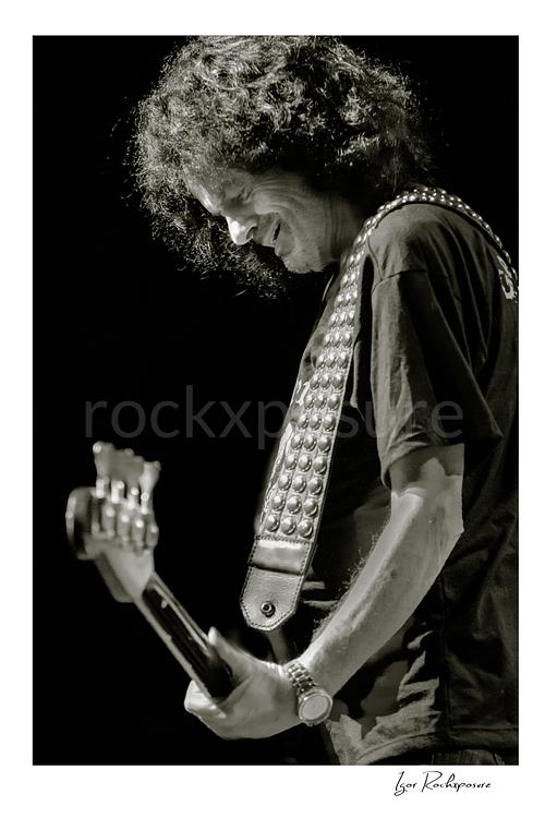 Vertical black and white image of Jimmy Bain of Last in Line playing bass onstage in a quiet live performance portrait