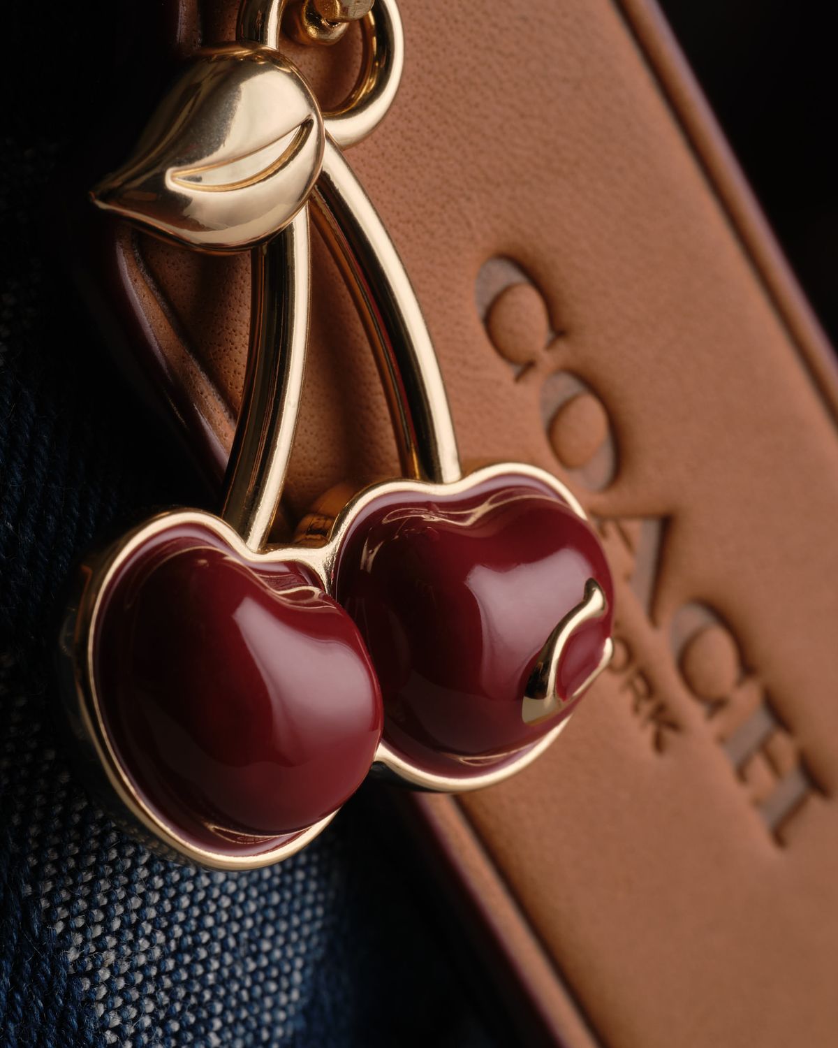 Deep red and gold cherry shaped charm hanging on a designer purse