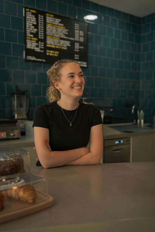 A café owner standing behind the counter, smiling while working in the coffee shop