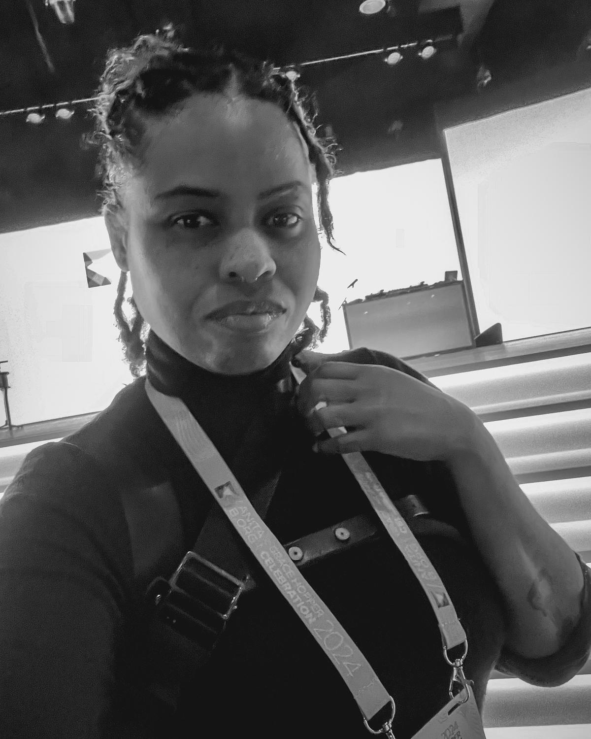 Andriana Ortiz, founder of Emmages, backstage at the 2024 Grace Hopper Celebration. Captured in black and white, this candid self-portrait highlights her presence, awareness, and strategic proximity as a corporate event photographer.