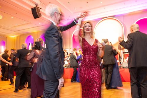A man twirls a woman in a red dress at the vibrant Bundespresseball 2024 dance floor.
