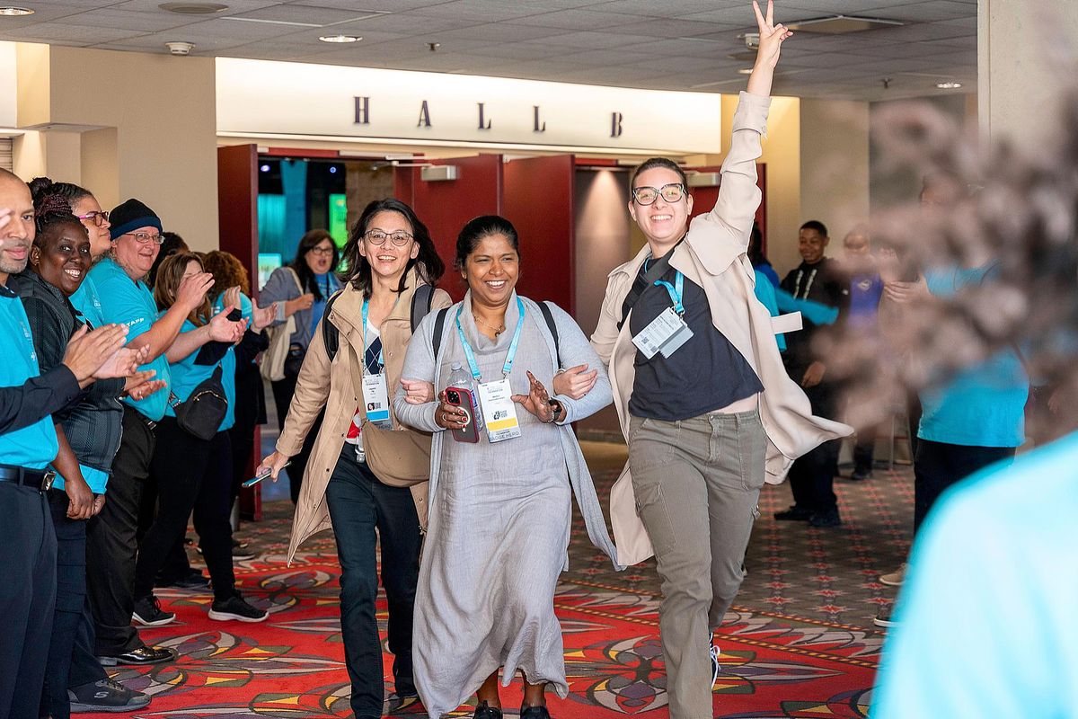 Corporate event photography capturing attendees walking through a high-energy welcome tunnel at the Grace Hopper Celebration 2024 in Philadelphia, emphasizing inclusion, community, and collective excitement within the tech space.