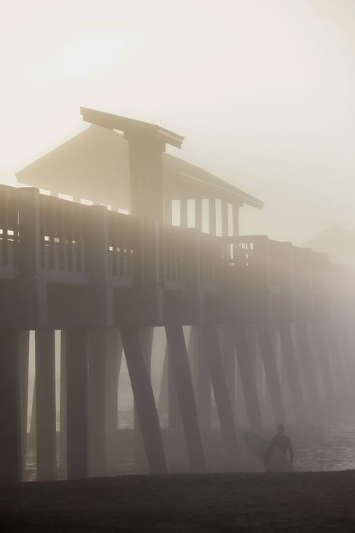 Surfer Walking Under the Pier in Morning Mist