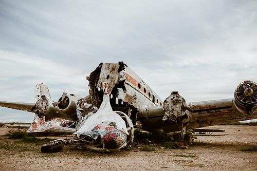 Empowered boudoir portrait of woman in wearing a parachute skirt, by a rusted, abandoned airplane.