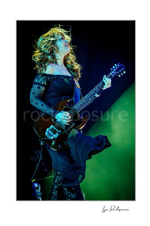 Vertical color image of Nancy Wilson performing with electric guitar during a Heart concert, with flowing hair and vivid green stage light