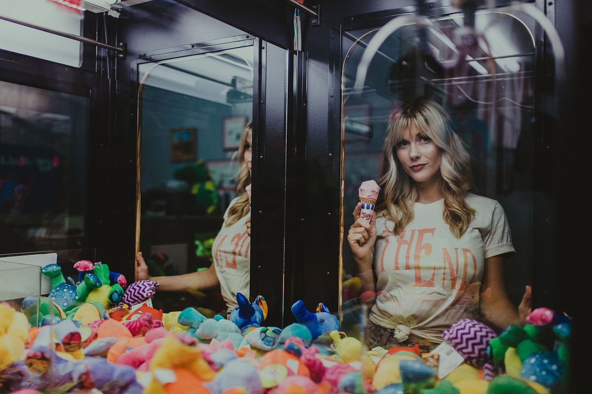 un, flirty photo of woman holding ice cream next to a retro claw machine.