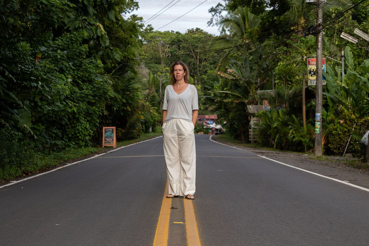 Milj&ouml;portr&auml;tt i dokument&auml;r stil: kvinna st&aring;r mitt p&aring; v&auml;g med tropisk gr&ouml;nska och bebyggelse runtom.