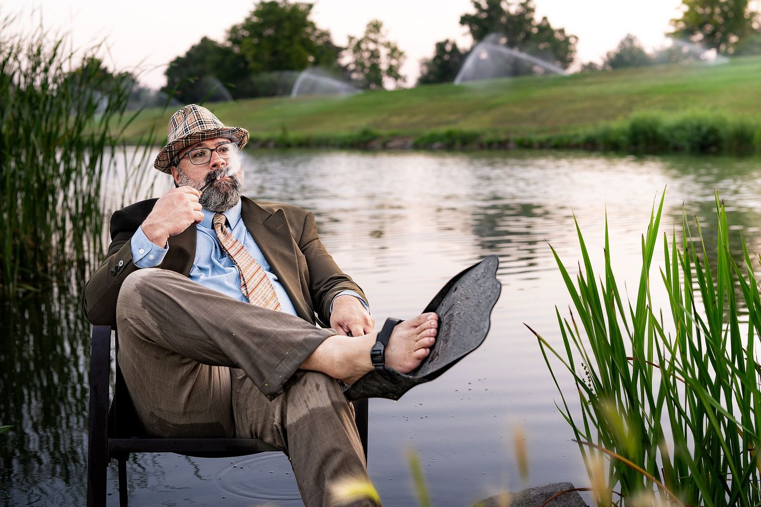 Portrait of a man in suit smoking a pipe, sitting on chair in lake, editorial