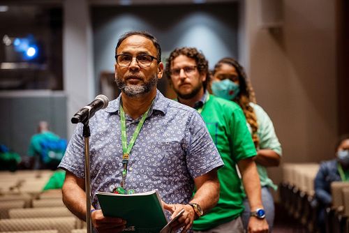 A union delegate speaks during an open forum at the AFSCME 45th International Convention in Philadelphia, addressing members while standing in line with others wearing green shirts.