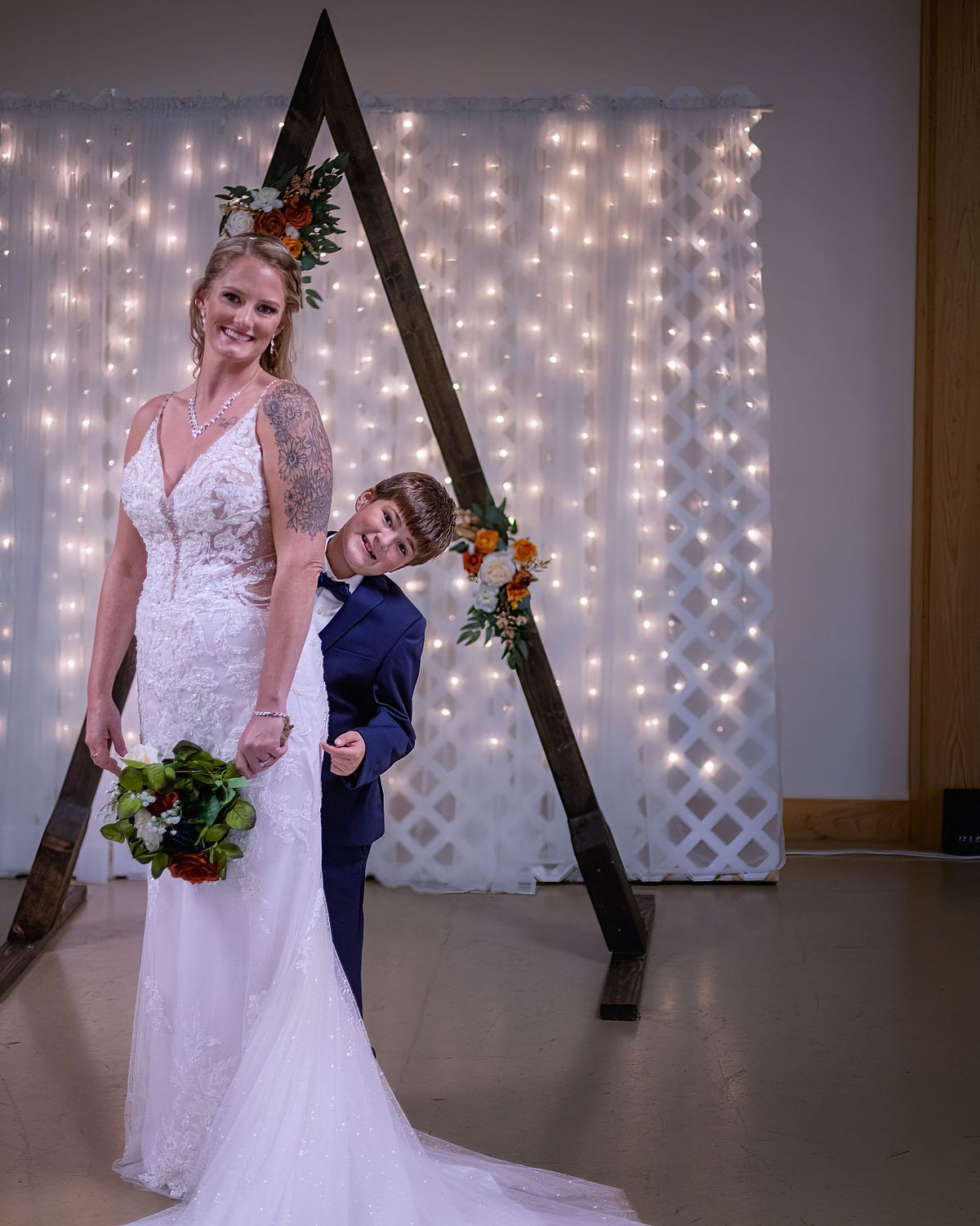 fun pose of bride with her son inside ross station, the son is peaking around his mom, the mom is smiling and holding flowers