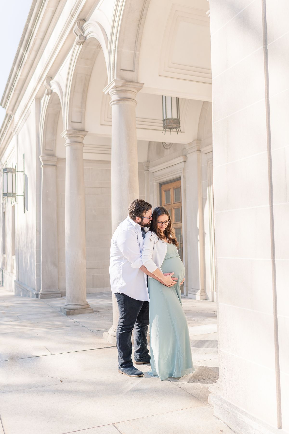 Expectant couple holding her pregnant belly outside arches of The Frick Museum
