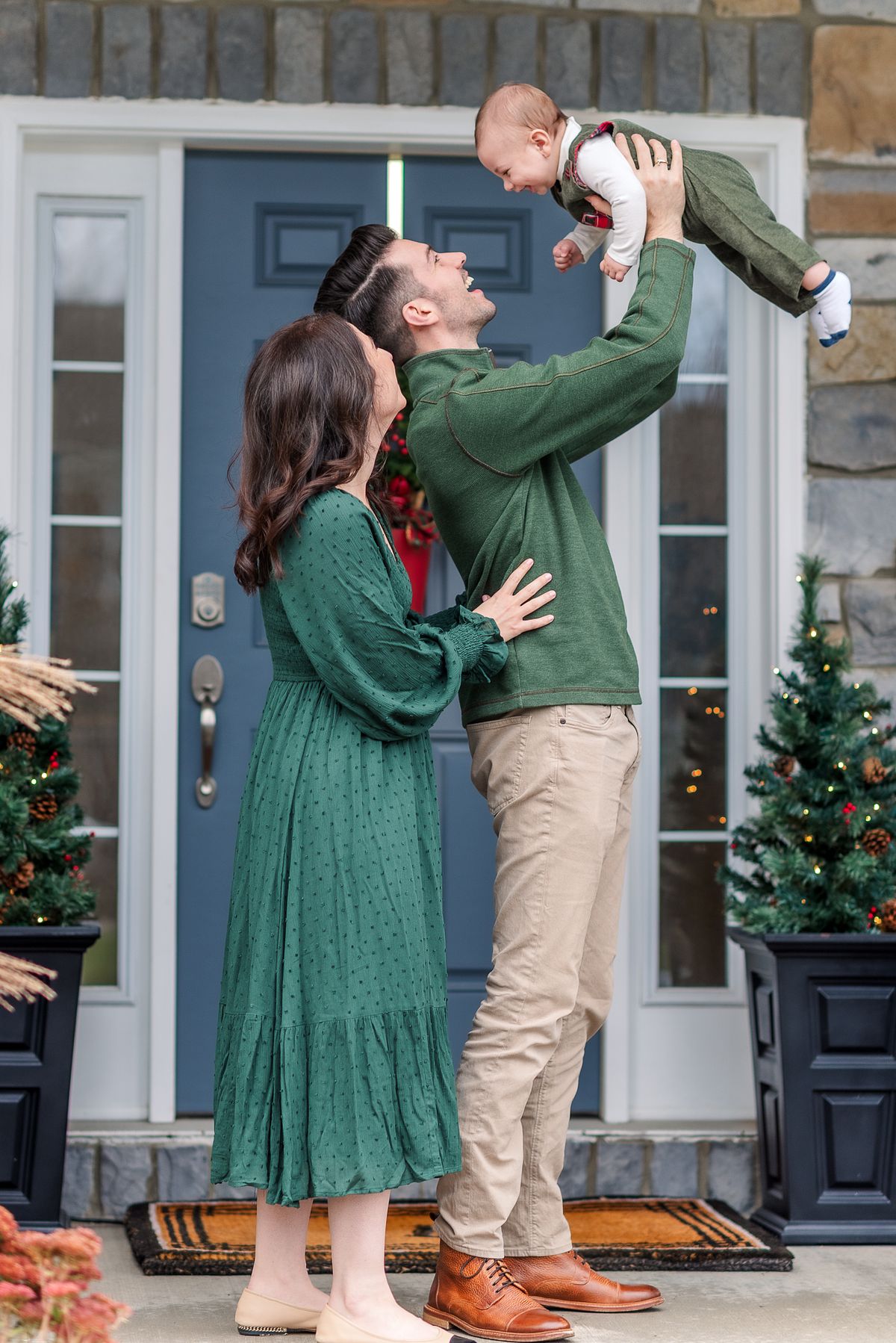 Husband holding baby up high and smiling at him with wife behind him looking on happily with Cranberry Township, PA newborn photographer