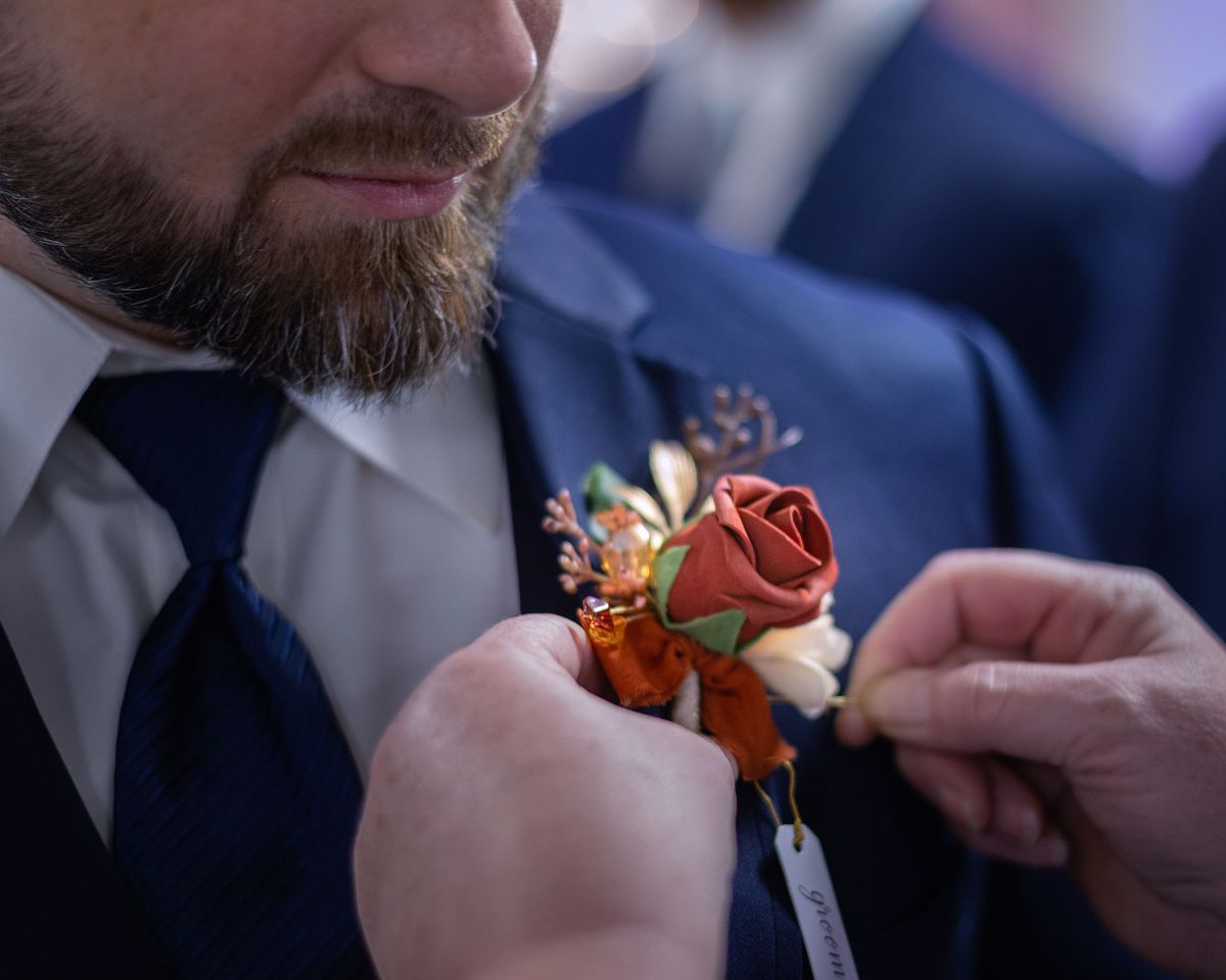 groom looking at his suit while getting flowers pinned on his label