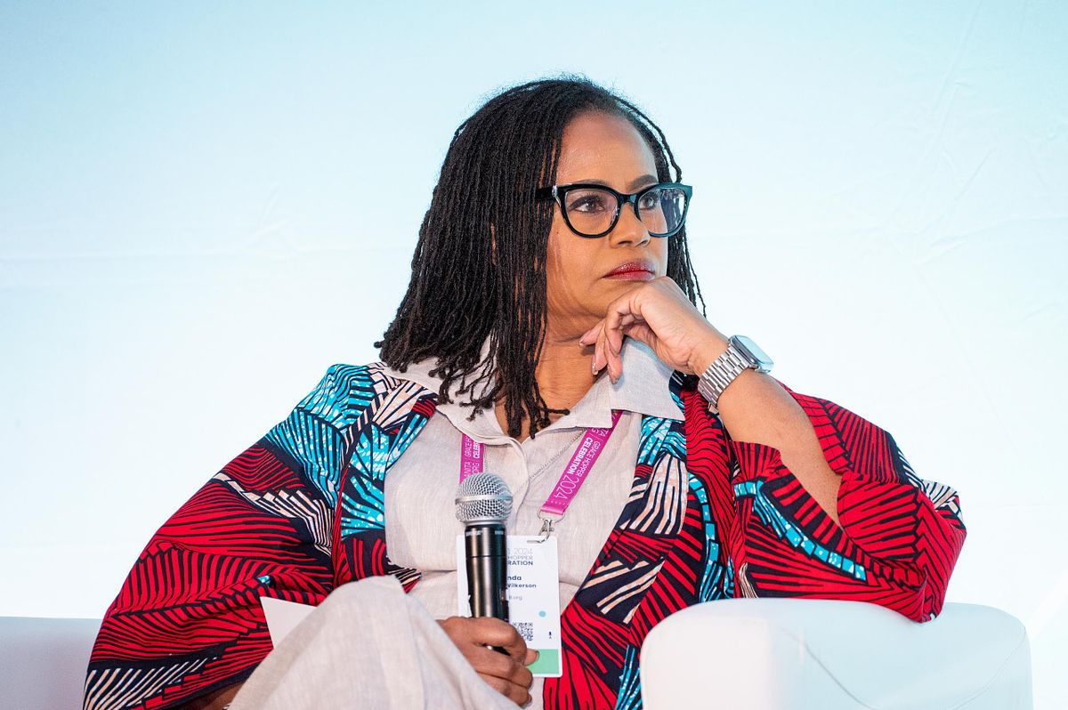A keynote speaker sits thoughtfully on stage holding a microphone during a corporate leadership panel discussion at a professional conference.