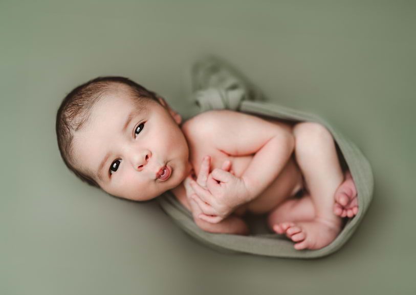 Swaddled newborn baby peacefully sleeping in a green wrap, photographed by Houston newborn photographer Amanda Mandola.
