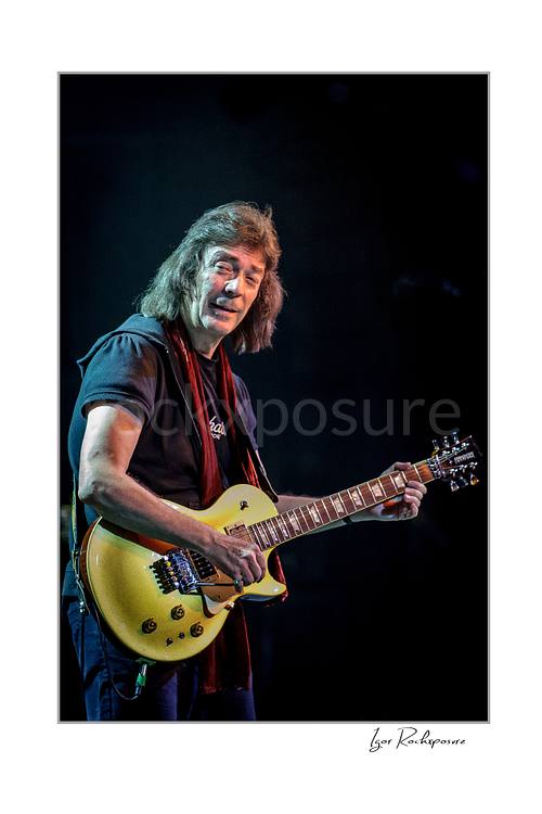 Vertical color image of Steve Hackett performing live with electric guitar in a close-up stage portrait