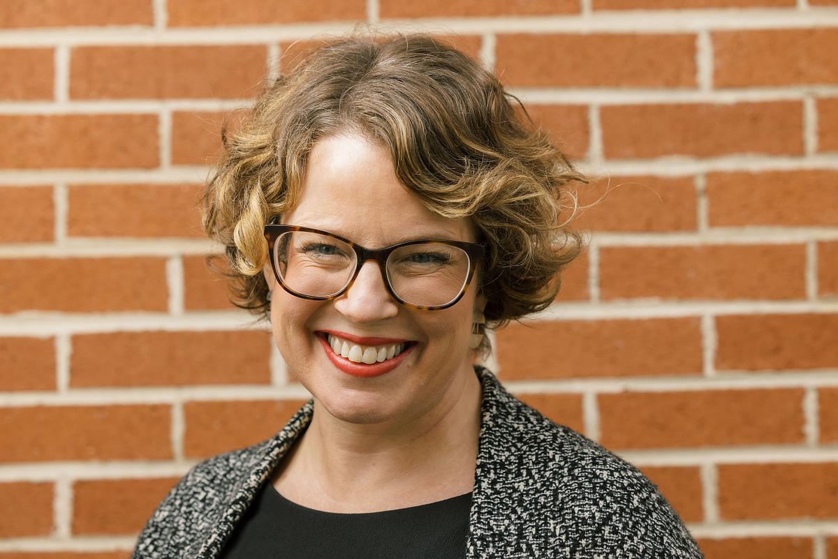 A close-up headshot a woman against a brick backdrop at an outdoor location in Carrboro, NC