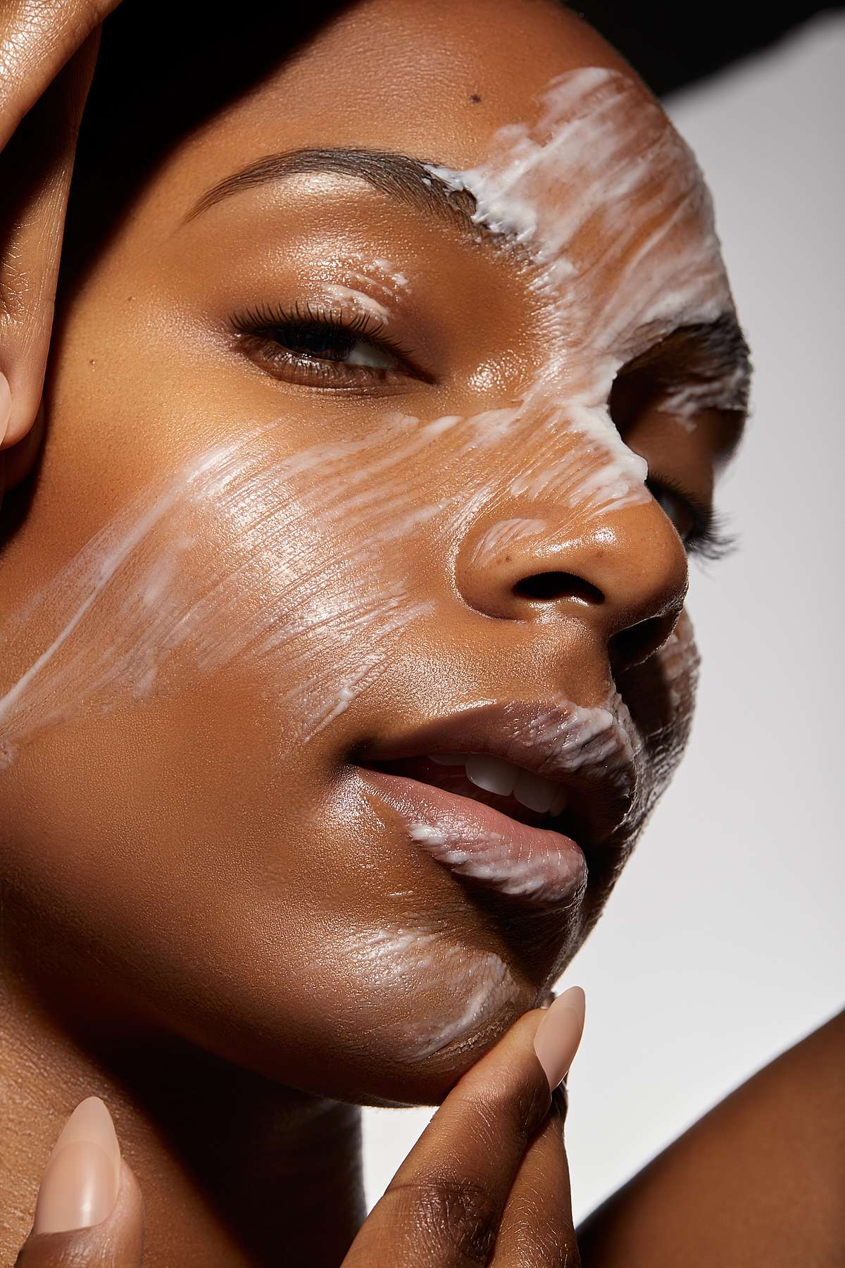 Close-up of a woman's face with white foam cleanser being massaged onto her glowing skin.