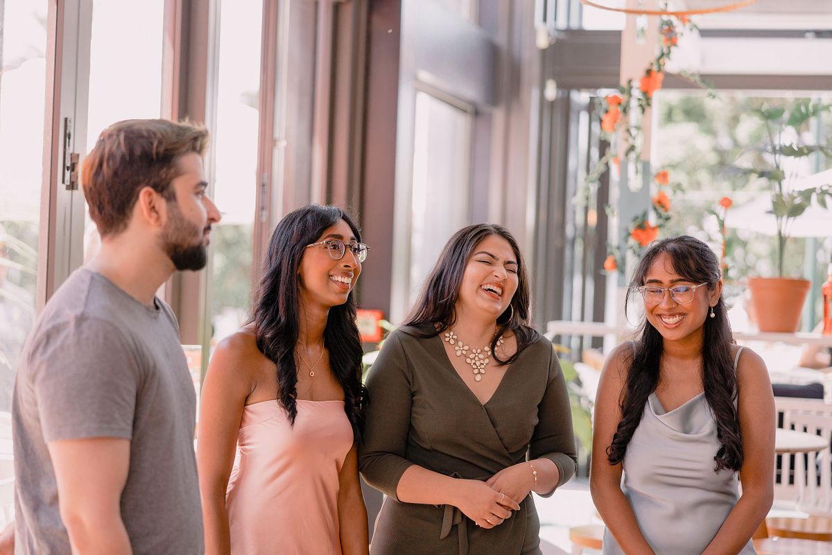 Photographer in Basel capturing a group of four people at an engagement party in a well-lit room, smiling and laughing. The atmosphere is joyful and relaxed, with orange flowers in the background.