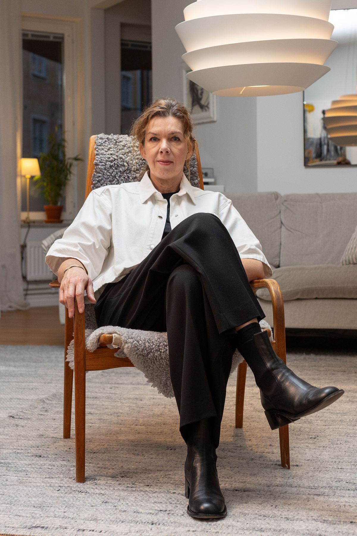 Person sittande i f&aring;t&ouml;lj i ett skandinaviskt vardagsrum med modern taklampa och mjuka texturer.