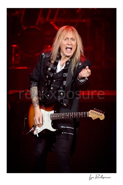 Vertical color image of Chris Caffery of Trans Siberian Orchestra performing live with an electric guitar against a red stage background