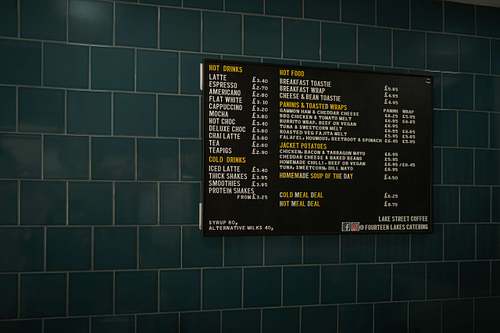 Café menu board mounted on a tiled wall inside an independent coffee shop