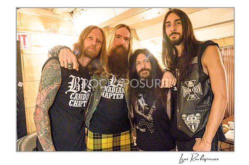 Horizontal portrait of the four members of Black Label Society standing closely together backstage, smiling and posing for the camera.