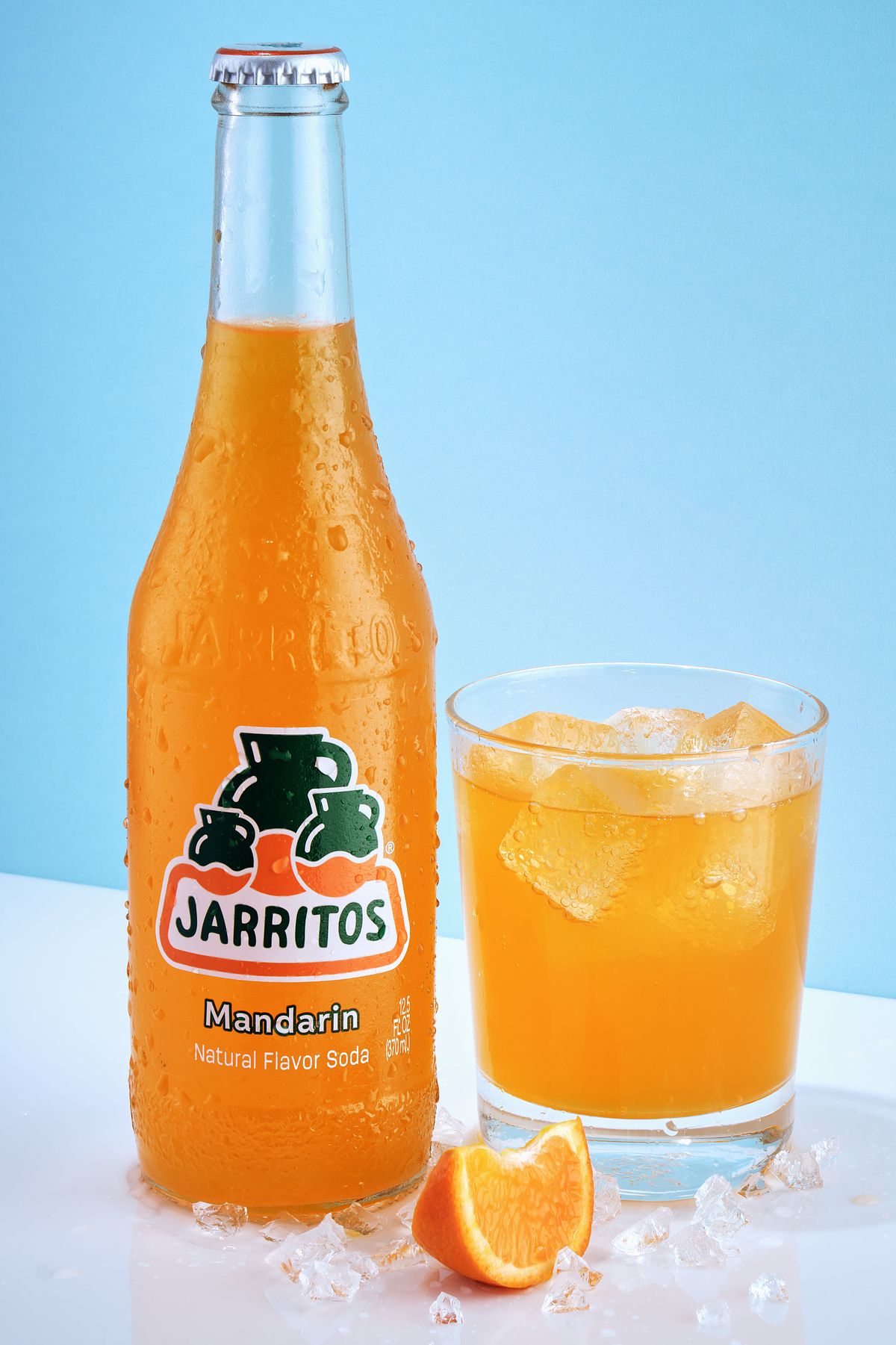 Spec Ad of a cold bottle of Jarritos Mandarin soda beside an iced glass of orange soda and a tangerine slice.