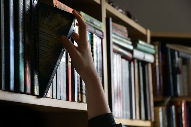 a person reaching for a book on a book shelf