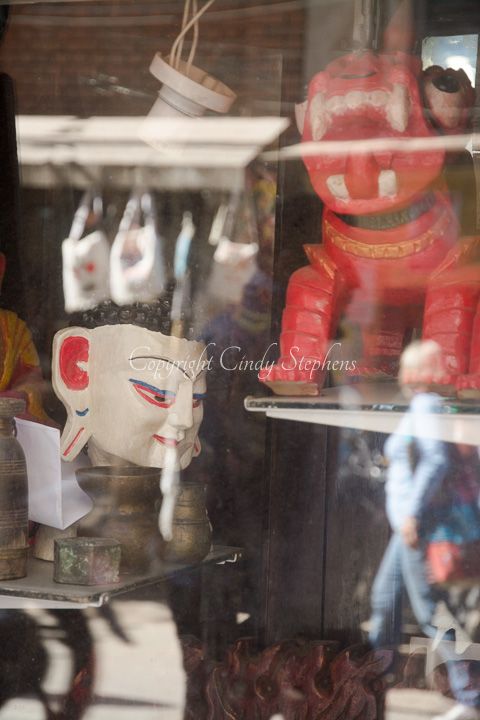 Reflection of a white cultural mask in Nepalese shop window, juxtaposed with the vibrant street scene of Kathmandu.