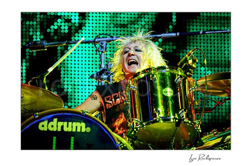 Horizontal color image of James Kottak of Scorpions playing drums live with wild blond hair and bright green stage lights