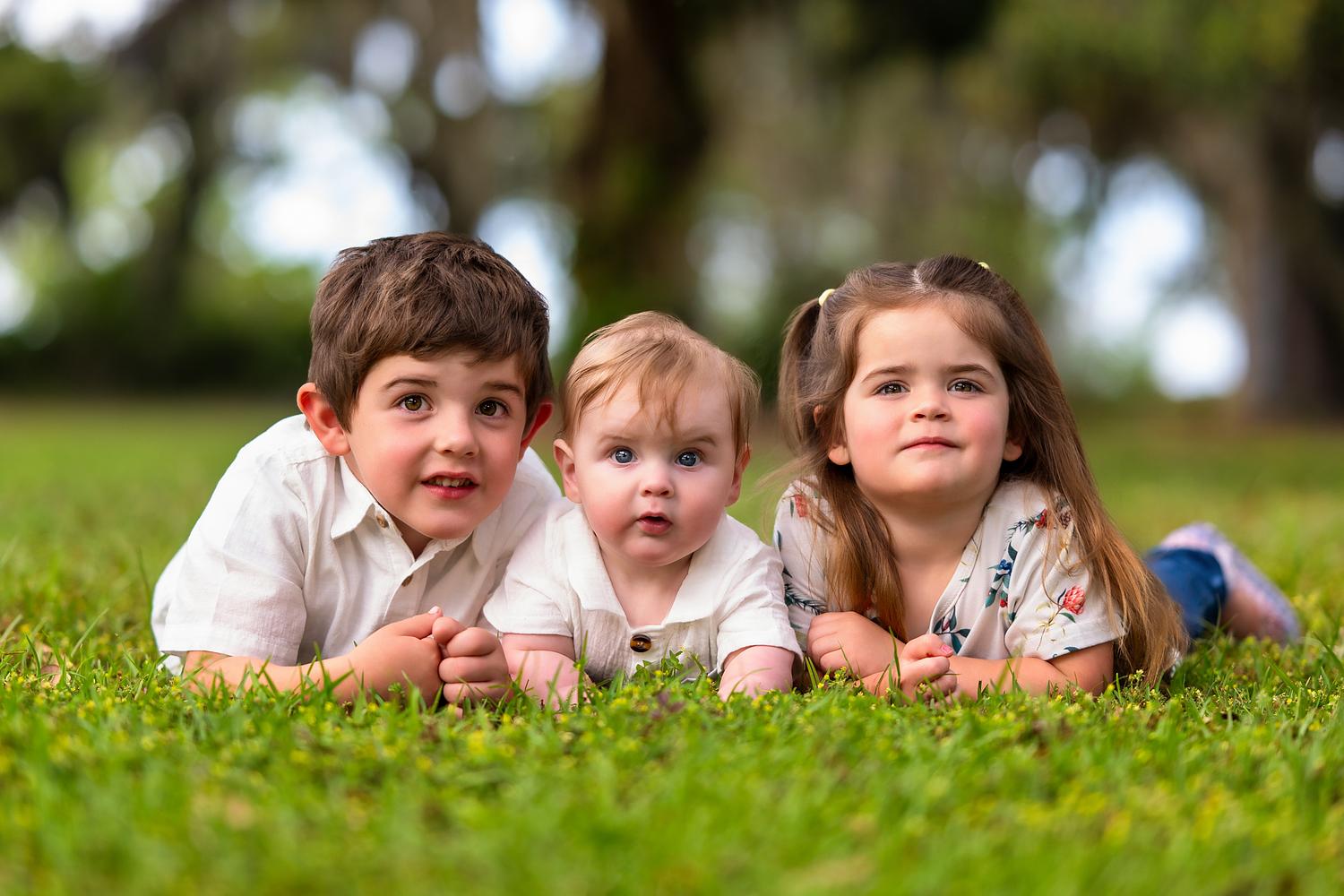 Three young children lying side by side and looking at the camera during a professional family photography session in Beaufort, South Carolina.