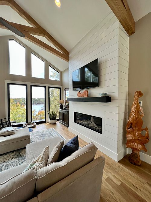 Close up view of gas fireplace which is clad in shiplap and framed in by ceiling mounted wood trusses.