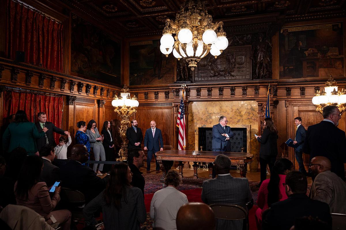 Pennsylvania governor&rsquo;s office event with leadership team and attendees gathered in an ornate state room before a bill signing, photographed with a wide editorial perspective showing audience, staging, and environment
