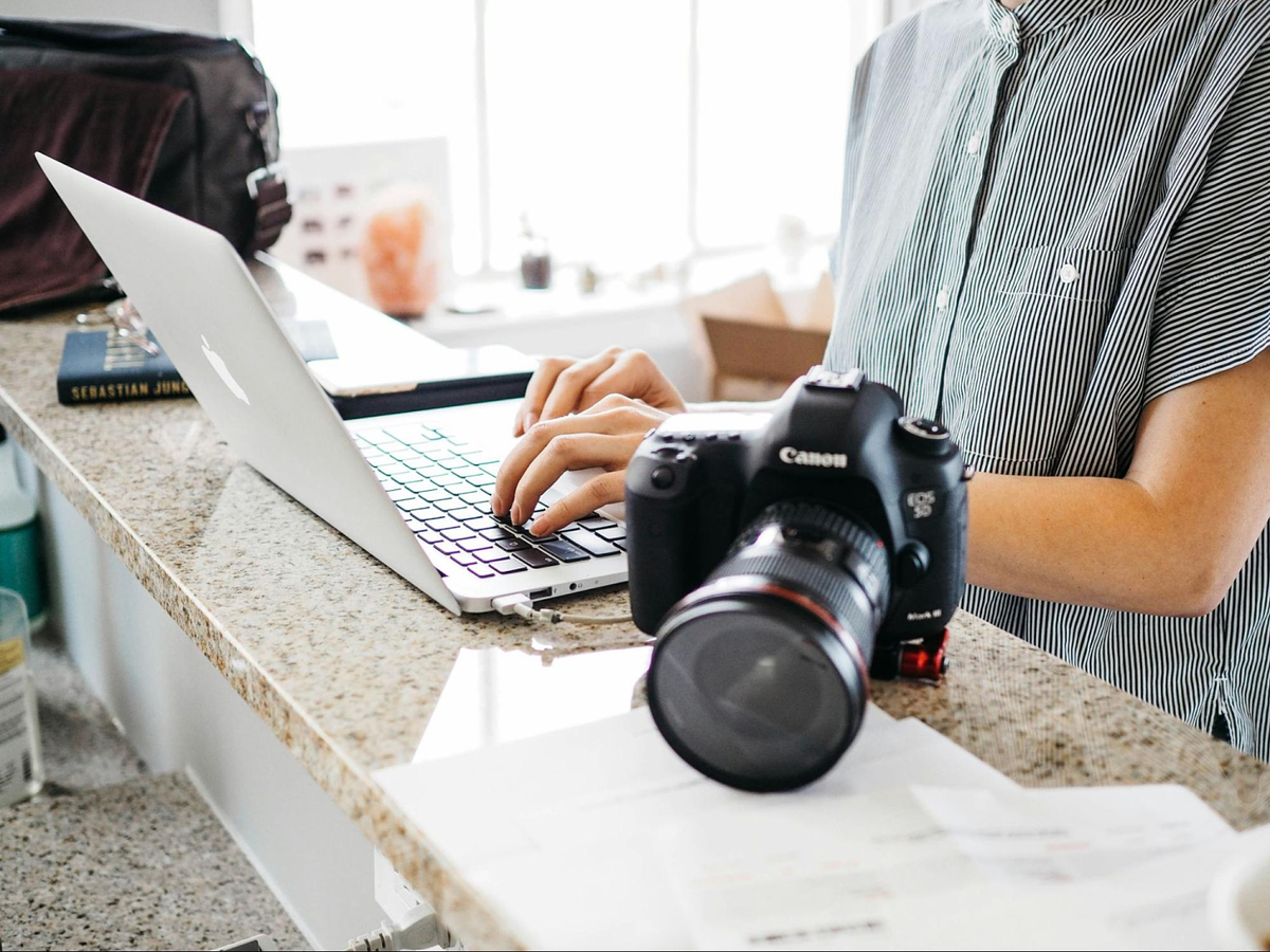 a person typing in a laptop keyboard with a canon camera on top of the marble table